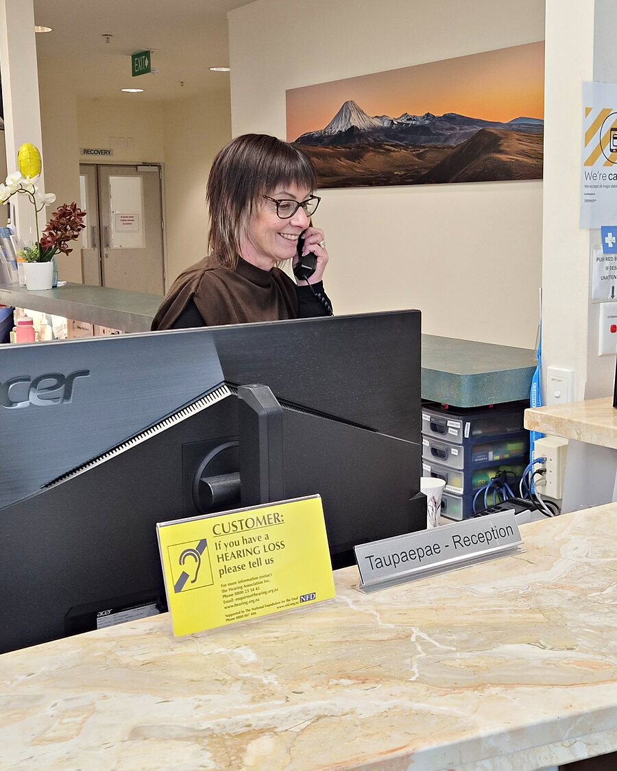 A Belverdale Hospital receptionist smiling while taking a phone call at the Taupaepae reception desk